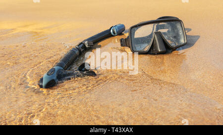 Sole che splende al nero di snorkelling e immersioni subacquee maschera sulla spiaggia bagnata sabbia lavata dal mare. Foto Stock
