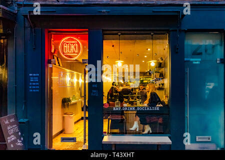 Una donna si siede ad un tavolo vicino alla finestra illuminata in Boki, un caffè indipendente in Seven Dials, Londra, Regno Unito Foto Stock