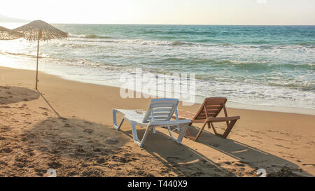 Vuoto due lettini di plastica rivolta verso il tramonto e il mare in background. Immagine che illustra vacanza tropicale. Foto Stock