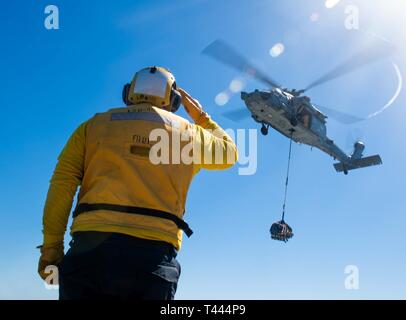 OCEAN (16 marzo 2019) di Boatswain Mate 2a classe John Robert Davis Jr. saluta il pilota di un MH-60S Sea Hawk elicottero, attaccato al mare in elicottero Combat Squadron (HSC) 21 come esso si diparte la harpers Ferry-classe dock anfibio sbarco nave USS harpers Ferry (LSD 49). Harpers Ferry è in corso conducendo le operazioni di routine come una parte di USS Boxer anfibio gruppo pronto (ARG) nell'Oceano Pacifico orientale. Foto Stock