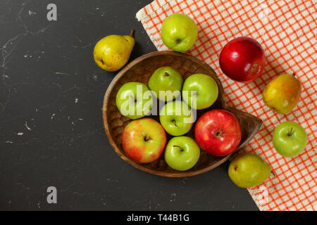 Foto da sopra - le mele e le pere in legno scolpito ciotola sul marmo nero come la scrivania con la tovaglia Foto Stock