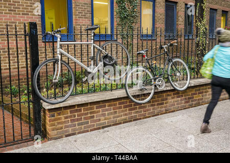 Vecchie biciclette bloccato alla recinzione metallica, elevata al di sopra del suolo, offuscata persona passando su un marciapiede Foto Stock