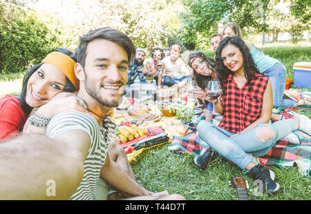 Gruppo di amici prendendo un selfie nel parco in una giornata di sole - le persone felici avente un picnic di mangiare e di bere il vino durante l'assunzione di foto Foto Stock