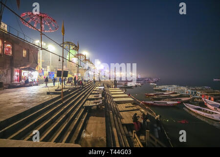 Varanasi Gange fiume ghat di notte con architettura antica e barche di legno allineate lungo la riva del fiume Foto Stock