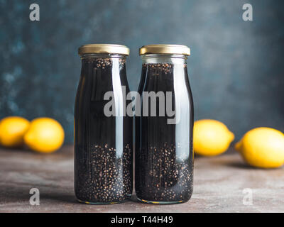 Detox carbone attivo nero acqua chia o limonata con il limone. Due bottiglie di nero chia infusa l'acqua. Detox drink idea e ricetta. Vegan cibi e bevande Foto Stock