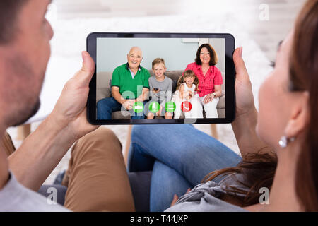 Giovane seduto sul divano una videoconferenza con la loro famiglia felice con tavoletta digitale Foto Stock