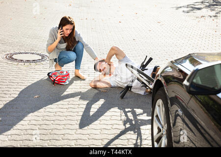 Giovane donna chiamando ambulanza dopo colpire ciclista maschio accidentalmente con la sua automobile Foto Stock