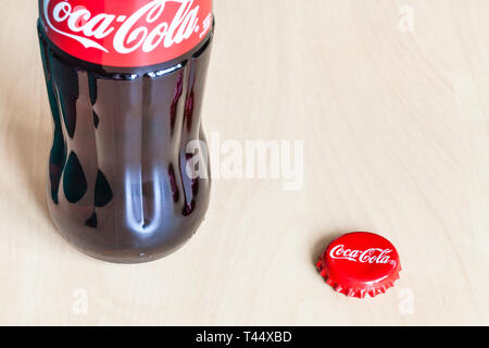 Mosca, Russia - aprile 4, 2019: una bottiglia di vetro e usato crown cork tappo di bottiglia di Coca Cola bevanda sul pannello di legno. La coca cola (coke) è addizionata di anidride carbonica in modo Foto Stock