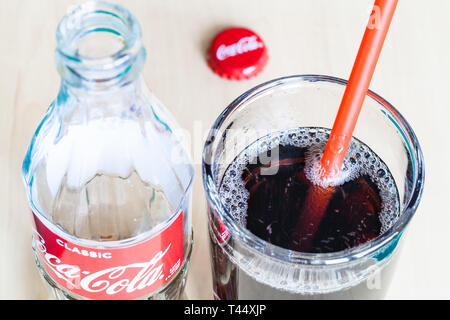 Mosca, Russia - aprile 4, 2019: bere in vetro rosso con cannuccia e la bottiglia vuota di Coca Cola bevanda sul tavolo. La coca cola (coke) è gassata Foto Stock