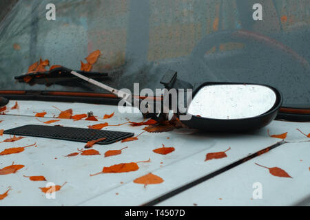 Sul cofano di una vecchia auto arrugginito è rotto specchietto laterale e foglie di autunno. concetto Foto Stock