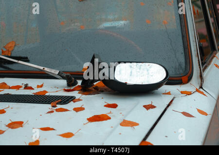 Sul cofano di una vecchia auto arrugginito è rotto specchietto laterale e foglie di autunno. concetto Foto Stock