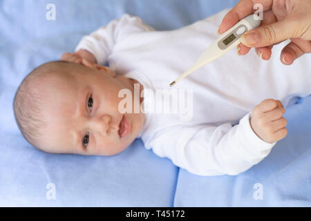 Madre misura la temperatura del neonato con il termometro digitale. Bambino il concetto di salute. Foto Stock