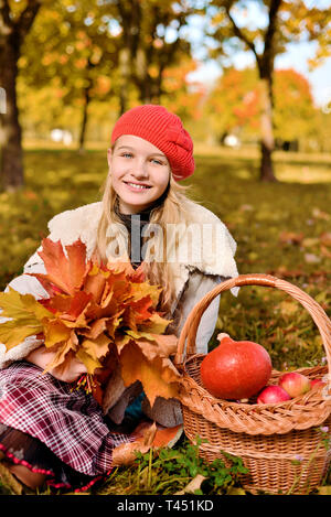 Felice adolescente sorridente. Autunno Ritratto di giovane e bella ragazza in Red Hat. Sullo sfondo si erge il cestello con mele e zucca, ombrello giallo Foto Stock