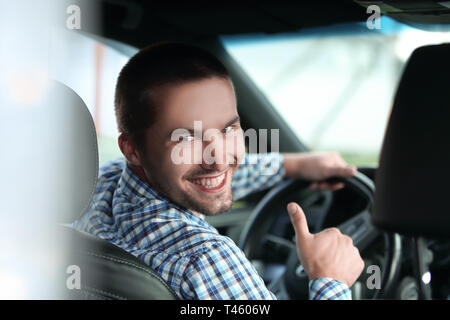 Close up. l uomo moderno seduto in un auto e mostrando il suo pollice in alto. Foto Stock