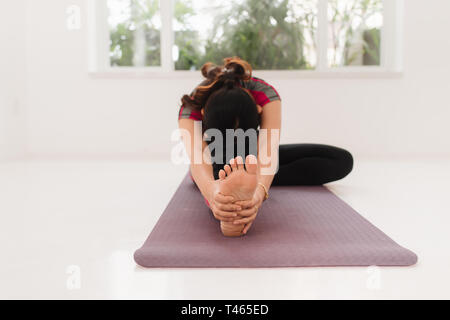 Giovani attraenti yogi donna a praticare yoga concetto, in seduta Janu Sirsasana esercizio, testa a ginocchio piegare in avanti pone, lavorando da indossare nero spo Foto Stock