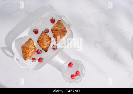 Croissant con lamponi. I lamponi con croissant. Croissant su uno sfondo luminoso con bacche di lampone Foto Stock