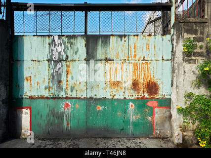 La colorata Vecchia rusty ingresso gate metallico mostrato in Iloilo City, Filippine, al giorno. Situato dietro il cancello è un entità industriali. Foto Stock