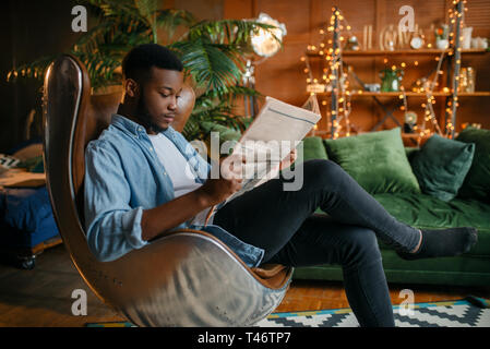 Uomo nero leggendo il giornale in una sedia confortevole Foto Stock