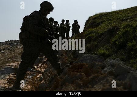 Marines con Charlie Company, Battaglione Team di atterraggio, 1° Battaglione, 4 Marines, cercano il coperchio mentre assaltando una posizione difensiva durante un live-Incendio campo come parte del trentunesimo Marine Expeditionary Unit simulati Expeditionary avanzate operazioni di base, Camp Schwab, Okinawa, in Giappone, 13 marzo 2019. Marines con il trentunesimo MEU stanno conducendo EABO simulato in una serie dinamica di eventi di formazione per affinare le loro capacità di pianificare, provare e completare una varietà di missioni. Durante EABO, il trentunesimo MEU ha collaborato con la terza divisione Marine, 3° Marine Logistics Group e il primo velivolo Marina Wing e una Foto Stock