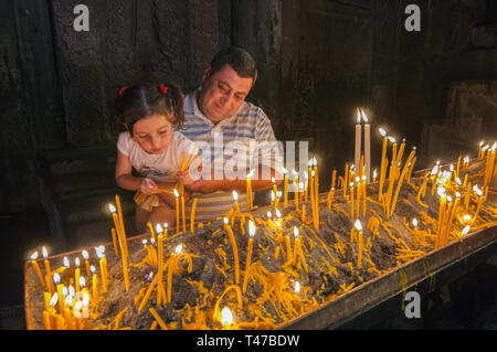 Armenia, Goght, persone di preghiera di illuminazione candele in rock-cut camera del Monastero di Geghard, fondata 4 c da Gregorio l Illuminatore presso il sito di un sac Foto Stock