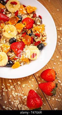 Tabella immagine superiore di sani di fiocchi d'avena e fatti in casa con ingredienti di fragole e mescolare i frutti nella piastra bianca sul tavolo da pranzo in legno. Foto Stock