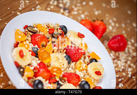 Tabella immagine superiore di sani di fiocchi d'avena e fatti in casa con ingredienti di fragole e mescolare i frutti nella piastra bianca sul tavolo da pranzo in legno. Foto Stock