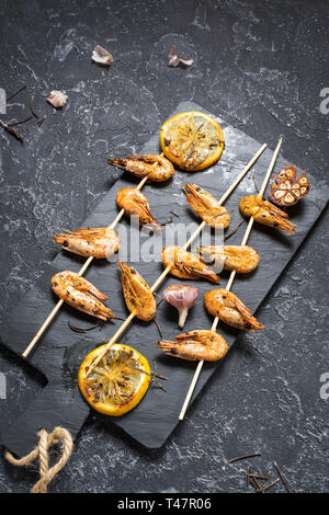 Grigliate gli spiedini di gamberi con erbe aromatiche, aglio e limone su pietra nera dello sfondo. Frutti di mare, shelfish. Foto Stock