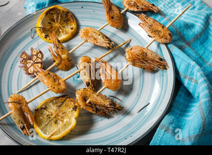 Grigliate gli spiedini di gamberi con erbe aromatiche, aglio e limone sul cemento dello sfondo. Frutti di mare, shelfish. Foto Stock