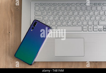 Moderno e dal design di computer notebook o laptop e smartphone, mobile con triple fotocamera nella luce di una tavola di legno Foto Stock