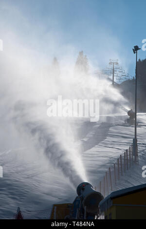 Il pittoresco foto verticale di bianco artificiali nuvole di neve, rendendo dalla macchina neve, sulla giornata di sole. La preparazione di piste in una montagna sciistica, durante w Foto Stock