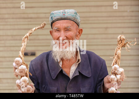 Anziani uyghur uomo con barba aglio tiene nelle sue mani. Catturato in un mercato di Kashgar (provincia dello Xinjiang, Cina) Foto Stock