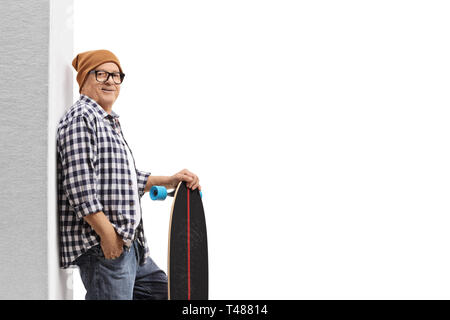 Uomo maturo hipster con un longboard appoggiato contro una parete isolata su sfondo bianco Foto Stock