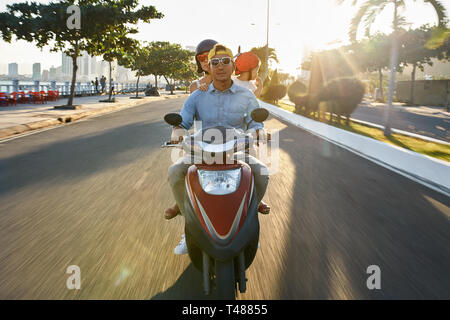 I genitori con il loro bambino in sella motocicletta sulla soleggiata città street Foto Stock