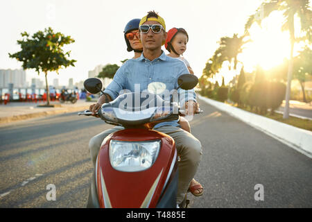 I genitori con il loro bambino in sella motocicletta sulla soleggiata città street Foto Stock