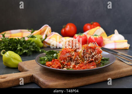 Peperoni ripieni di carne e riso e salsa di pomodoro situato in una piastra su sfondo scuro Foto Stock