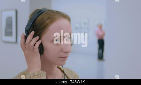 Donna che guarda la esposizione, utilizzando le cuffie e ascolto audio guida Foto Stock