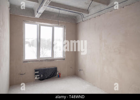 Stanza vuota con una finestra e una batteria in una casa in costruzione, pareti intonacate, un massetto sul pavimento, calcestruzzo multi-livello di lastre. Concetto di r Foto Stock