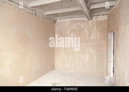 Camera a vuoto in una casa in costruzione, pareti intonacate, battuto sul pavimento, calcestruzzo multi-livello di lastre. Il concetto di riparazione nella nuova casa, ov Foto Stock