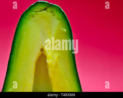 Vista parziale di mezzo taglio avocado close up sul magenta sfondo rosa. Vividi colori vibranti. Foto Stock