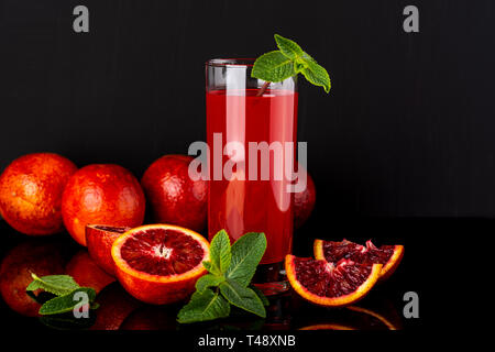 Bicchiere di succo di frutta con alcuni pezzi del siciliano di colore arancione su sfondo nero. Siciliano di bevanda a base di arancia. Foto Stock