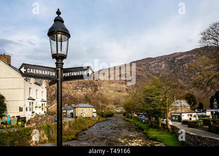 Lampada con segnaletica per porthmadog & Caernarfon sul ponte del fiume in Beddgelert, Galles il 9 aprile 2019 Foto Stock