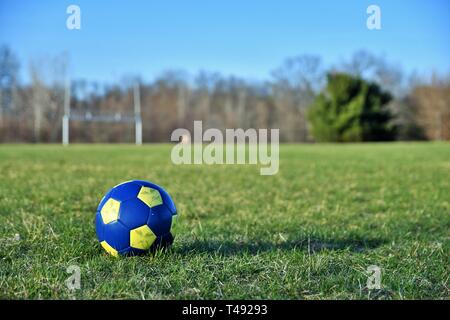 Close up di un blu e giallo pallone da calcio in primavera con un campo in background Foto Stock