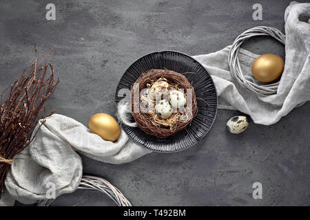 Pasqua laici piatta su sfondo scuro con uova di quaglia nel nido, biancheria fabrique e due uova d'oro scuro su sfondo a trama Foto Stock