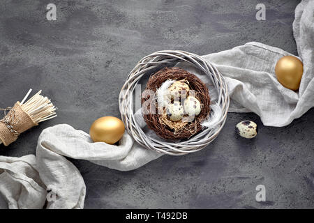 Pasqua laici piatta su sfondo scuro con uova di quaglia nel nido, biancheria fabrique e due uova d'oro scuro su sfondo a trama Foto Stock