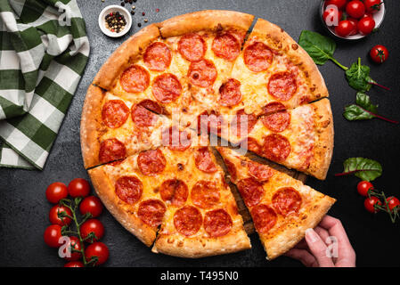 Salsiccia per pizza pizza su un calcestruzzo nero lo sfondo. Raccolta a mano fetta di salsiccia per pizza pizza. Tabella vista dall'alto. Parte cibo, fast food concept Foto Stock