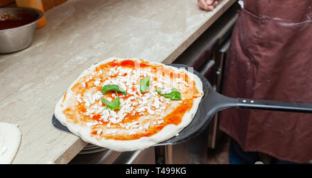 Materie pizza margherita messo sulla pala da forno per la cottura. Foto Stock