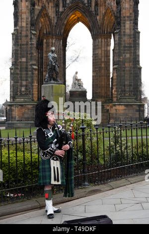 Scottish uomo che indossa un kilt e suonare la cornamusa di fronte al monumento di Scott per autore di Sir Walter Scott, Edimburgo, Scozia Foto Stock