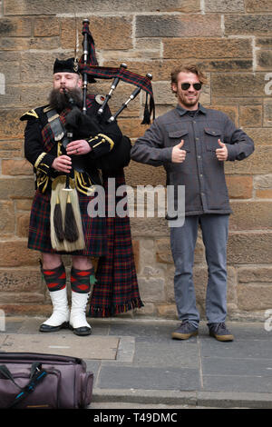 Tourist in posa per una fotografia accanto a un uomo suonare la cornamusa indossando un tradizionale kilt scozzese Foto Stock