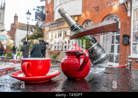 Un rosso brillante tazzina, piattino Teiera e bottiglia di vino formano una vistosa centrotavola su un outdoor cafe tabella in Church Street, Windsor, Regno Unito Foto Stock