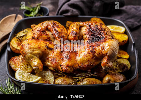 Tutto fritto tabaka pollo con le patate in una padella per grigliare, sfondo scuro. Foto Stock